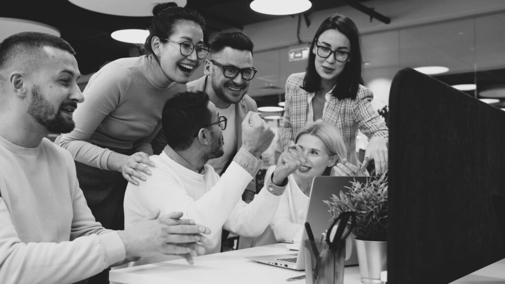 Un gruppo di cinque colleghi sorridenti e diversificati che collabora davanti a un computer in ufficio, rappresentando il concetto di employer branding e cultura aziendale positiva.