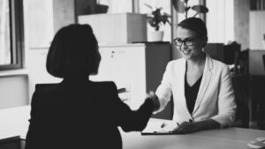 Due donne professioniste in ufficio che si stringono la mano cordialmente durante un colloquio di lavoro o una riunione strategica.